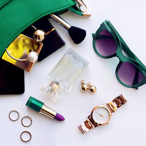 Top view of female fashion accessories . Green hanbag with  sunglasses,  gold watch , lipstick , perfume , rings , smartphone